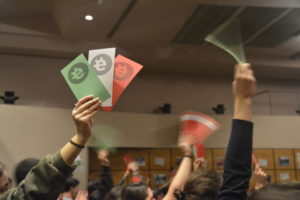 Arms of people holding voting cards, green, white and red, with Esplac's logo